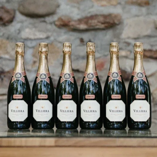 Six bottles of Villiera Brut Villiera Brut Natural 2021 sparkling wine against a stone wall.